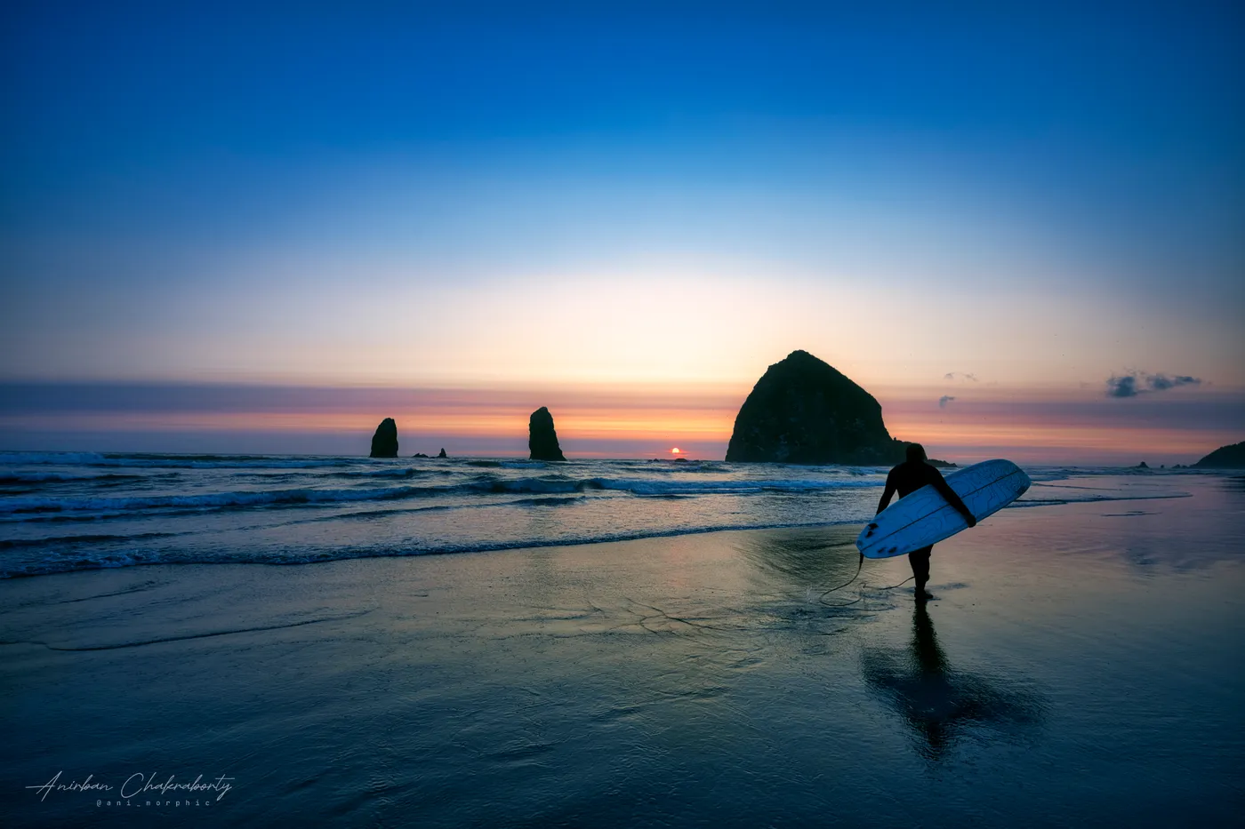 Carrying a board out past Haystack Rock at sunset