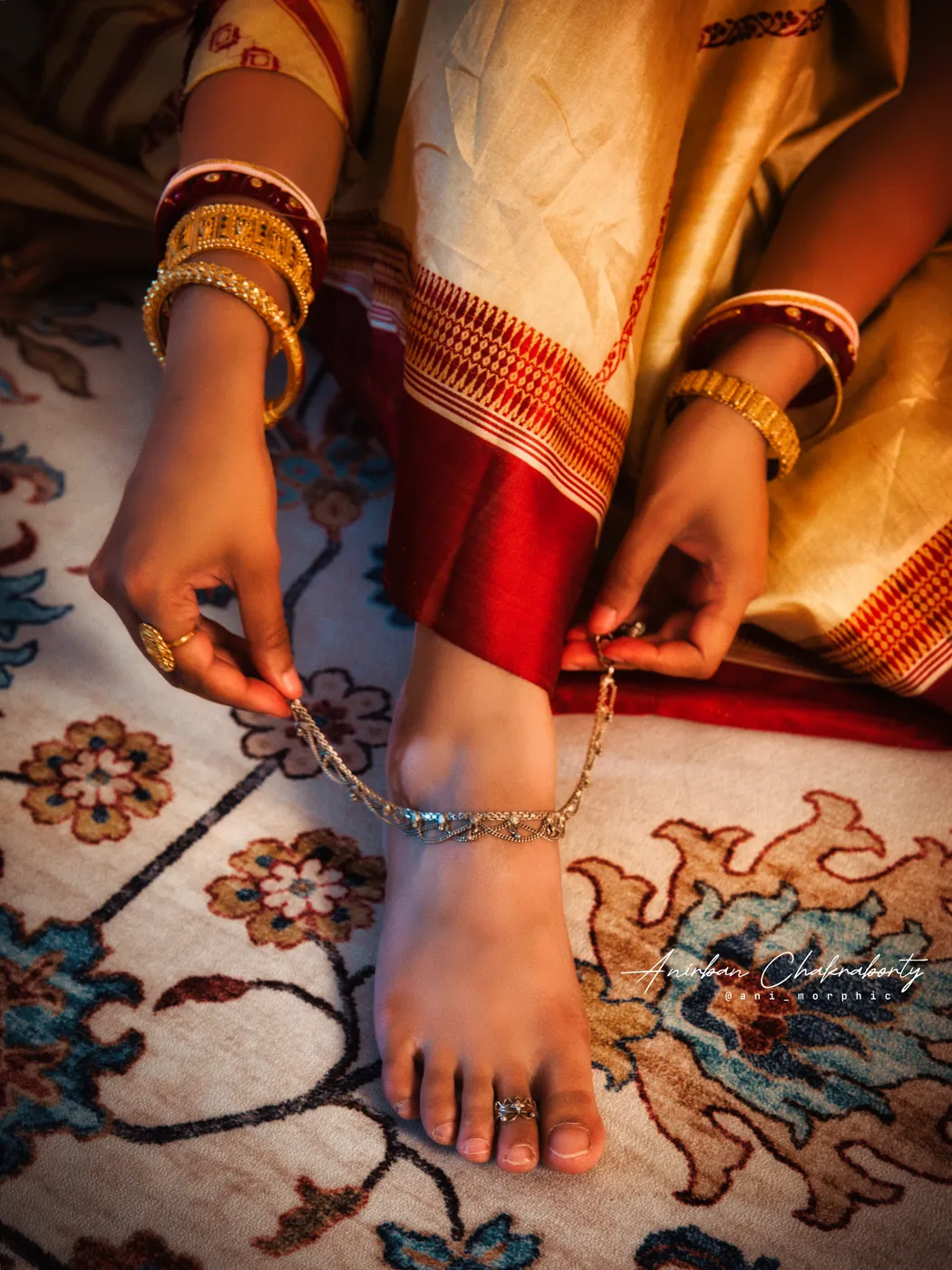 Fastening an anklet, gold against red and cream silk