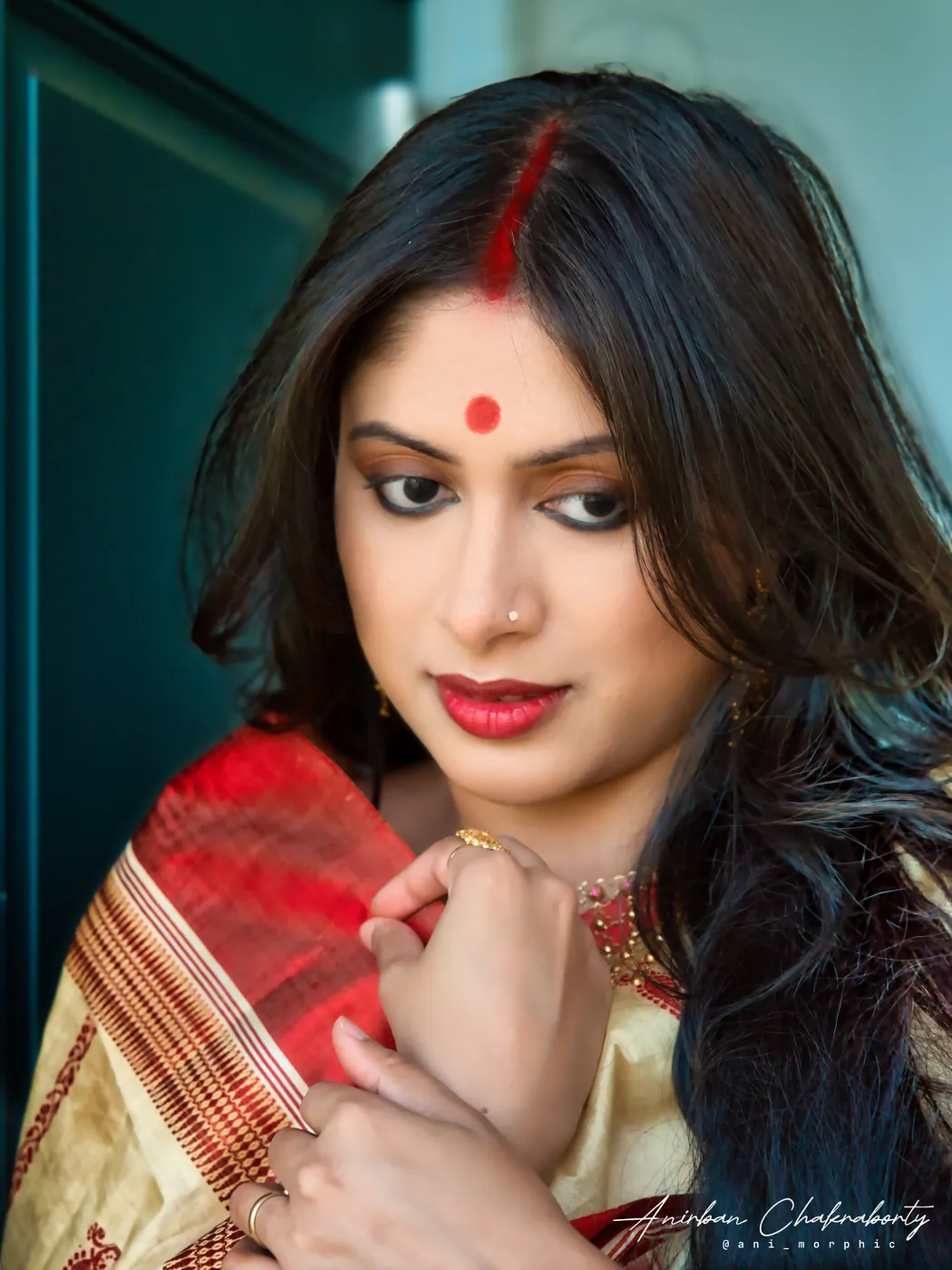 A red bindi, sindoor, and a hand holding the border of a saree