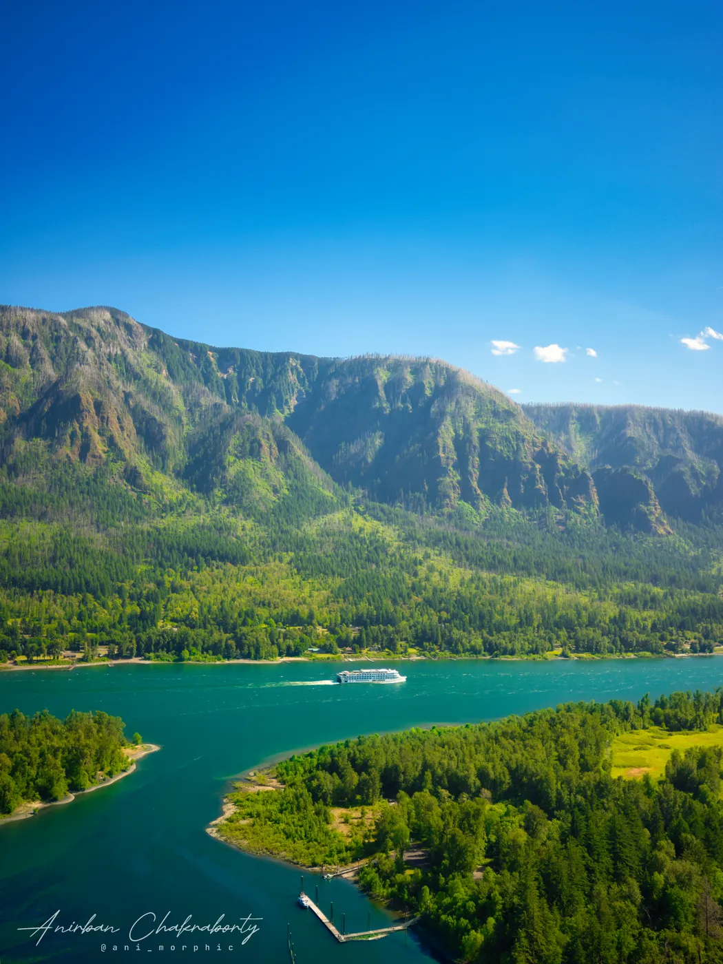 A cruise boat crossing the gorge below green cliffs