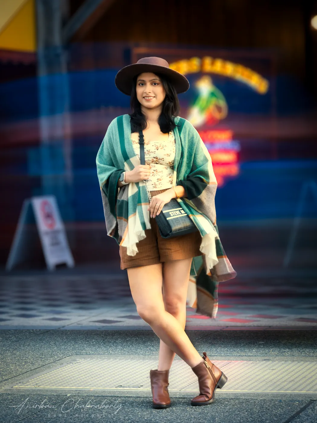 Wide hat and plaid on the boardwalk, neon coming on behind